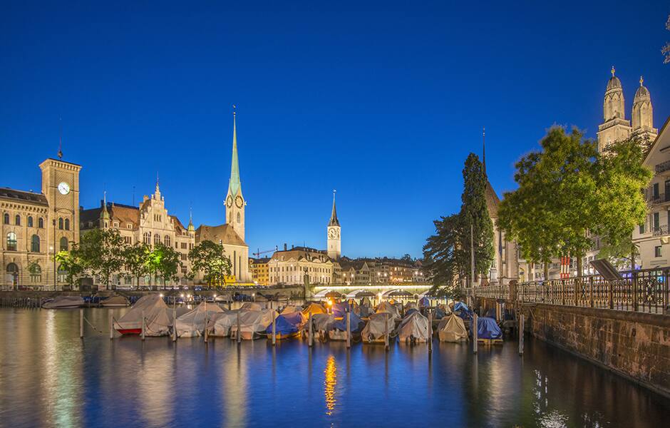 zurich skyline and boats with the church in the background on the limmat river at dusk