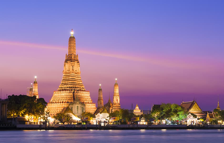 the illuminated temple of wat arun on the chao phraya river at sunset in bangkok thailand