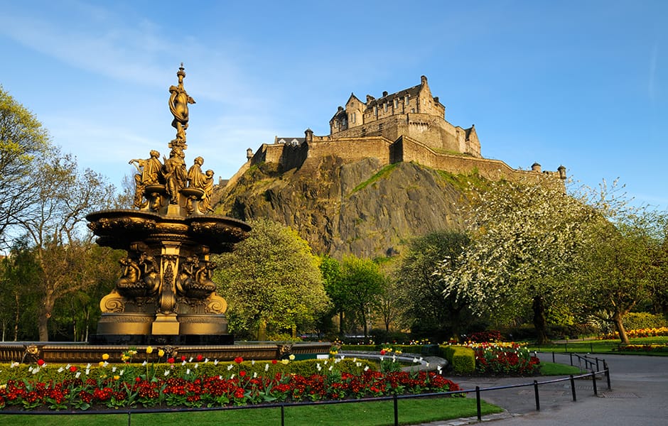 edinburgh castle pictured from princes street gardens on a sunny day with ross fountain in the foreground